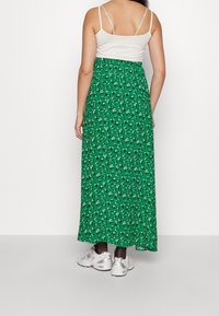 Jupe maxi verte à motifs floraux avec une taille ajustée et une silhouette fluide, associée à un débardeur blanc et des chaussures de sport argentées.