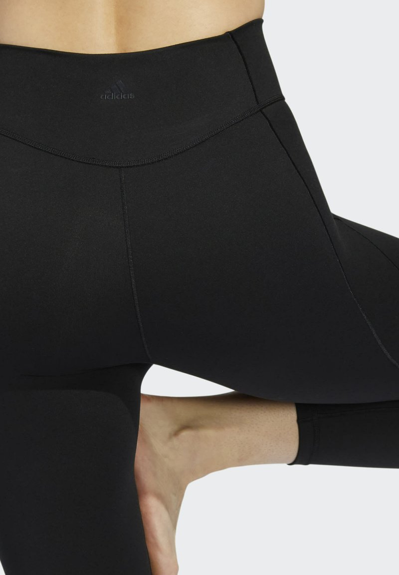 Leggings noirs taille haute en tissu lisse et extensible. Présentent des coutures plates et un logo discret sur la ceinture.