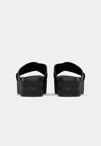 Černé platformové sandály s dvěma širokými pásky, hladkým materiálem a vyraženým označením "Calvin Klein Jeans" na podrážce.