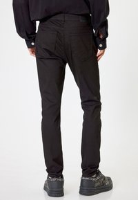 Musta slim-fit farkut, joissa on sileä pinta, varustettuna kahdella takataskulla ja huomaamattomilla ompeleilla. Yhdistetty mustiin teksturoituihin tennareihin.