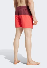 Costume da bagno rosso e bordeaux con vita elastica, coulisse e design a blocchi di colore, realizzati in un tessuto morbido e leggero.