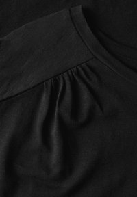 Top in tessuto nero con scollo rotondo, texture sottile e dettagli plissettati su una spalla. Finitura liscia e sensazione leggera.