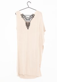 Robe tunique beige à coupe décontractée, présentant un détail en dentelle noire en forme de V au niveau du col, confectionnée dans un tissu doux et léger.