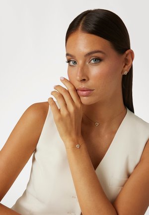Set di gioielli in oro con orecchini a forma di cuore, collana e bracciale con accenti di gemme. Texture liscia sulle catene d'oro.