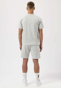 Světle šedé bavlněné tričko a odpovídající kraťasy, minimalistický design, krátké rukávy a kapsa na zadní straně kraťasů. Bílé tenisky s textem.