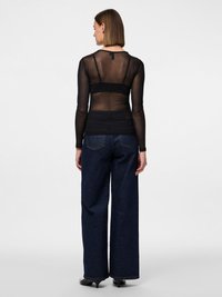 Czarna przezroczysta bluzka z długim rękawem z solidnym pasem w talii, zestawiona z wysokim stanem ciemnoniebieskich szerokich spodni i czarnymi szpilkami.