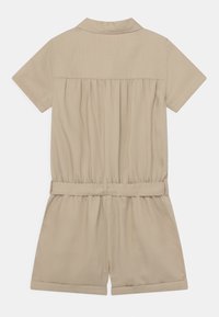 Beżowy kombinezon na krótki rękaw z miękkiego materiału, z kołnierzykowym dekoltem, marszczonym tyłem i materiałowym paskiem w talii.