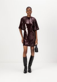 Robe mini en sequins bordeaux avec des manches bouffantes, associée à des bottes noires jusqu'aux genoux et un petit sac noir. Texture lisse et surface brillante.