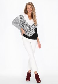 Szary, czarny i biały sweter w blokach kolorystycznych z cekinowym wzorem. Posiada dekolt w serek i długie rękawy, zestawiony z białymi spodniami w stylu dzwonów oraz czerwonymi botkami z frędzlami.