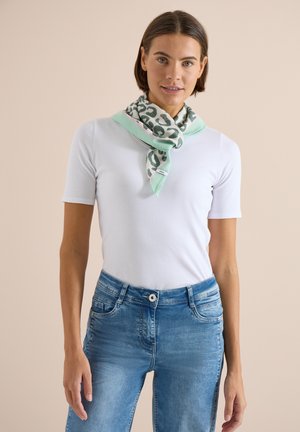 Donna che indossa una camicia bianca a maniche corte, jeans blu e una sciarpa verde menta con stampa leopardata legata intorno al collo.