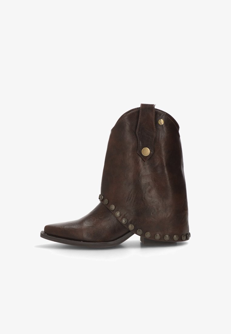 Botín de cuero marrón con punta afilada, adornos de metal alrededor de la base y un talón ligeramente elevado con una pestaña para una fácil colocación.