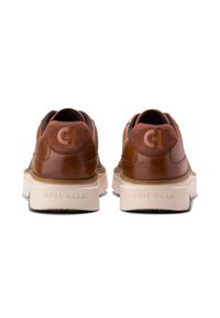 Hnědé kožené tenisky s hladkým povrchem a lehkou podešví. Mají embosované logo na patě a kontrastní design vzadu.