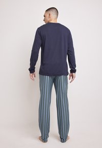 Camisa de manga larga en azul marino combinada con pantalones de pijama a rayas en tonos verdes y azules, con un corte relajado y una textura de tela suave.