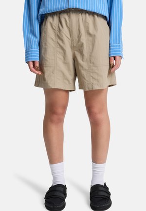 Beżowe krótkie spodenki do kolan noszone z niebieską koszulą w paski, białe skarpetki i czarne sneakersy na rzep na jednolitym tle.