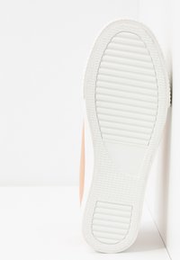 Podeszwa białego trzewika oparta pionowo na białej powierzchni, ukazująca teksturowane wzory bieżnika.