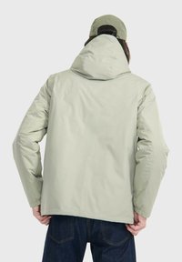 Hellgrüne, gefütterte Jacke mit Kapuze, die eine glatte Textur und elastische Bündchen hat, kombiniert mit einer passenden Mütze in der gleichen Farbe.