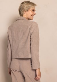 Beige Cord-Blazer mit kurzem Schnitt, Reverskragen und langen Ärmeln. Aus strukturiertem Stoff mit subtiler Rippenstruktur.