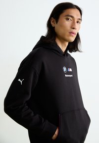 Sort hoodie lavet af blødt stof, med BMW og Motorsport logoer, Puma-logo på ærmet og en kængurulomme.