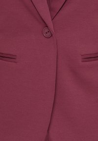 Gros plan d'un blazer rose foncé avec un bouton rose foncé fermé et deux poches fendues horizontales de chaque côté.