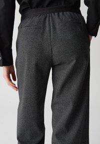Zwarte en grijze getextureerde broeken met een elastische tailleband, twee achterzakken en een losse pasvorm, met een subtiel ruitpatroon.
