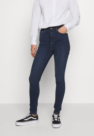 Skinny jeans van donkerblauwe denim met een hoge taille, met een slim fit, subtiele stiksels en voorkruiden, gecombineerd met zwarte sneakers.