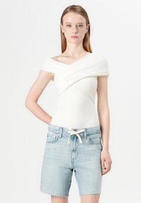 Off-white, lagerad bodysuit med axelband, parat med ljusblå denimshorts med dragsko och fransade kanter.