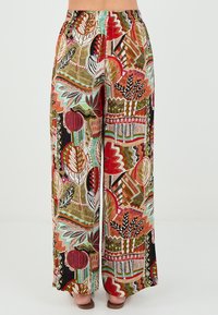 Pantalons larges et à motifs dans des couleurs vives de rouge, vert et beige. Présentent des designs abstraits, une taille élastique et un tissu fluide.