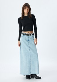 Zwarte lange mouwen crop top gecombineerd met een lichtblauwe denim maxi rok met een rafelige rand, en afgewerkt met een zwarte riem en enkellaarsjes.