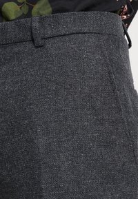Grijze op maat gemaakte broek van gestructureerde stof, met een platte voorkant, riemlussen en zijzakken, met minimale stikdetails.