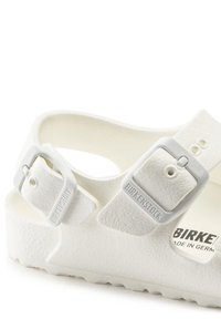 Białe sandały Birkenstock z dwoma regulowanymi paskami, teksturowanym materiałem i wyprofilowaną wkładką; wytłoczone logo na pasku.