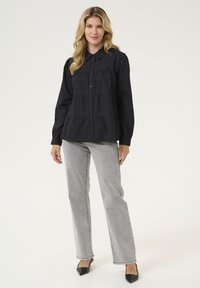 Camisa negra de botón con un diseño en capas, mangas largas y cuello clásico, combinada con jeans de cintura alta gris claro y zapatos negros.