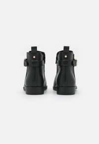 Bottines en cuir noir avec une texture lisse, dotées d'une sangle arrière et de petites accents en or. Semelles en caoutchouc plates.