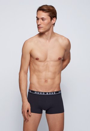 Zwarte katoenen trunk shorts met een witte "HUGO BOSS" logo tailleband, fitted ontwerp en gladde textuur. Model toont zijprofiel.