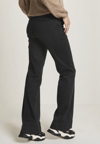 Svarta byxor med raka ben och slät textur, med lätt utsvängd fåll och kontrasterande sömmar. Matchas med tjocka svartvita skor.