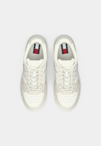 White sneakers featuring a mix of leather and suede materials, with perforated toe, tonal laces, and a logo featuring red and blue accents.