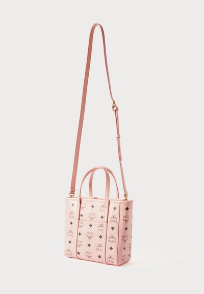 Mała różowa skórzana torebka na ramię z podwójnymi uchwytami u góry, regulowanym paskiem oraz powtarzającym się czarnym wzorem logo MCM po bokach.