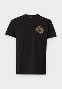 Tricou negru din bumbac, cu mâneci scurte și guler rotund. Prezintă un logo circular auriu pe pieptul stâng. Textură netedă.
