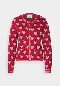 Punainen villatakki, jossa on vaaleanpunaisia sydänkuvioita, ribbausreunat, nappikiinnitys ja kaksi etutaskua. Valmistettu neulotusta kankaasta.