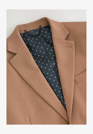Brauner Blazer mit scharfen Revers und einem strukturierten Stoff. Gefüttert mit dunkelblauem Stoff, der weiße Punkte aufweist. Enthält ein hängendes Kettendetail.