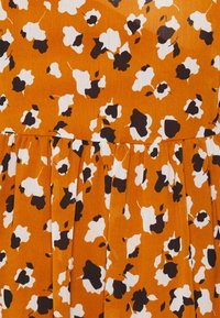 Oranssi kangas, jossa on valkoisia ja mustia kukkakuoseja, laskokset ja teksturoitu pinta. Sopii rentoihin vaatteisiin tai kesäasuihin.