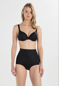 Svart trådløs bh med runde kopper og justerbare stropper, kombinert med høyhælte sorte shaping-truser med bølgete livlinje.