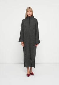 Gray knitted long dress with a high collar, wide sleeves, and side slits. Worn with red pointed flats.