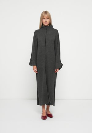 Gray knitted long dress with a high collar, wide sleeves, and side slits. Worn with red pointed flats.