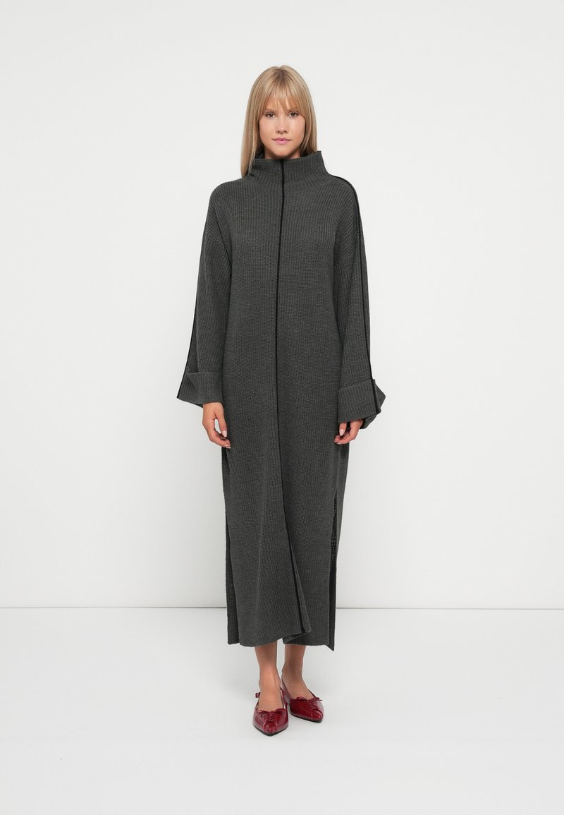 Gray knitted long dress with a high collar, wide sleeves, and side slits. Worn with red pointed flats.