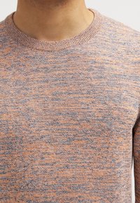 Maglione lavorato a maglia in rosa chiaro con motivo grigio screziato, caratterizzato da scollo tondo e superficie strutturata. Nessuna parte metallica visibile.