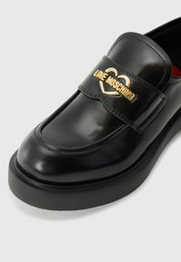 Black leather loafer with a rounded toe, a thick black sole, and a gold decorative strap featuring the text "LOVE MOSCHINO."