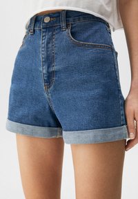 Donkere blauwe denimshorts met een licht vervaagde textuur, voorzien van een opgerolde zoom, voorzakken en een metalen knoopsluiting.