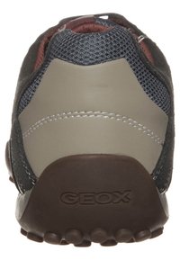 Bakre vy av en avslappnad sneakersko med mörkgrått mesh, en beige läderhäldpanel och en brun sula med präglingen av "GEOX"-varumärket.