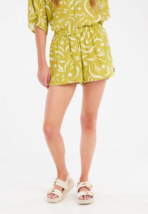 Shorts vert clair avec des motifs abstraits blancs, taille élastique ; associés à des sandales à plateforme beiges avec des accents de double boucle.