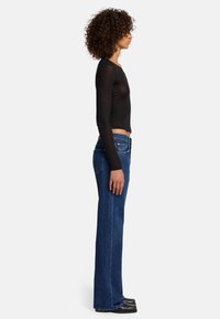 Maglietta nera a maniche lunghe e jeans a vita alta blu indossati da un modello, che mostrano una silhouette aderente, una texture in denim e una vita media.